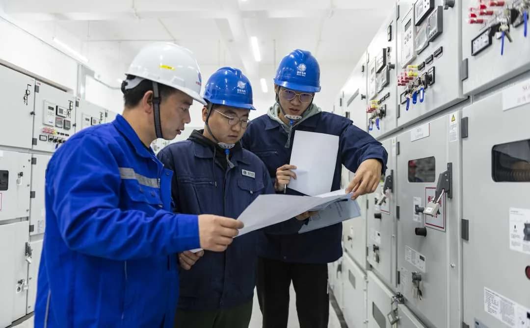 Engineering team reviewing electrical drawings beside switchgear.